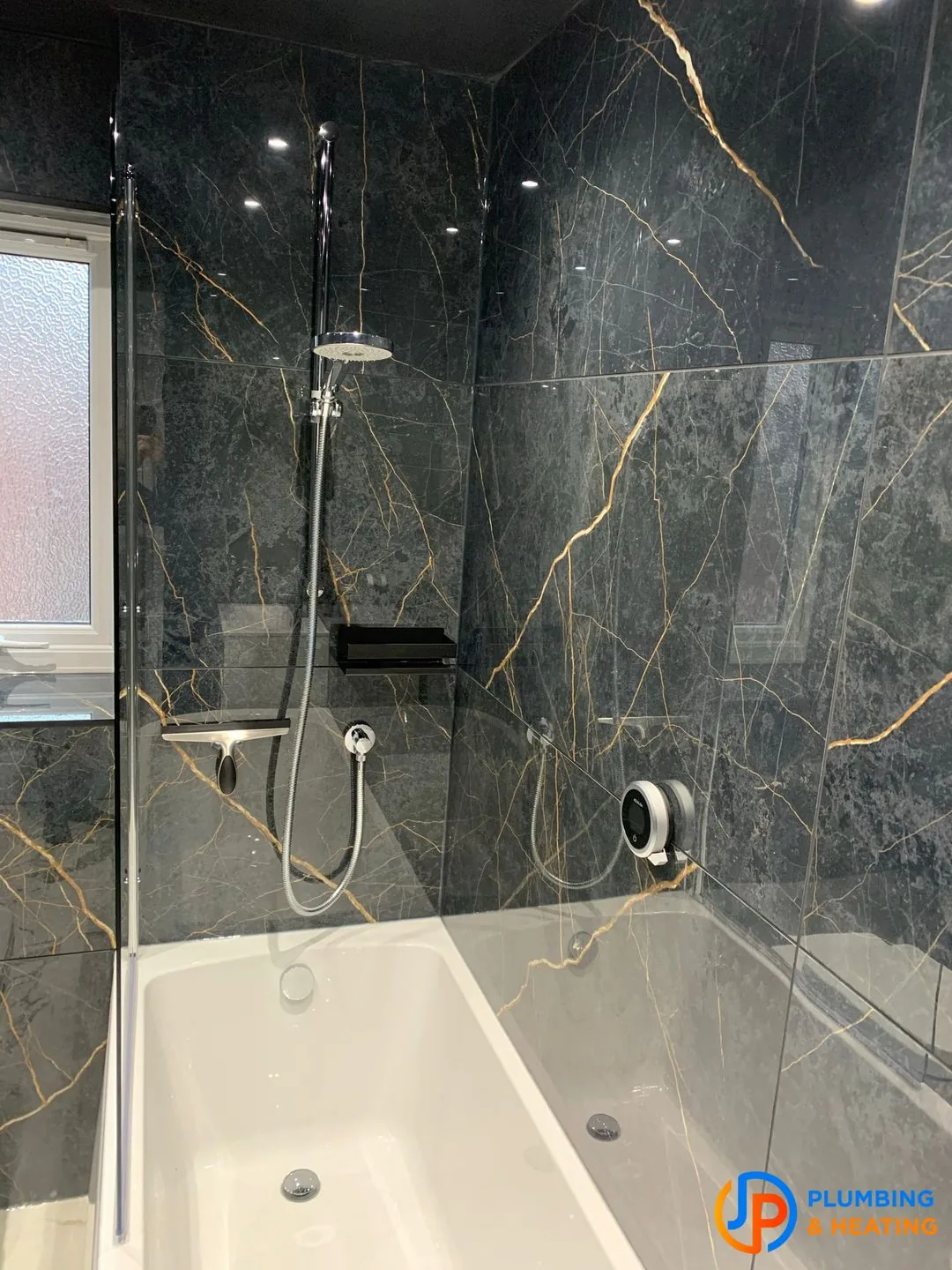 A bath with a shower over it, walled in black marble with gold veining, fitted by JP Plumbing and Heating
